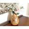 A handmade sunflower vase,  filled with faux daisies and zinnias, decorates a antique buffet table. The vase is made from a dried gourd. 
